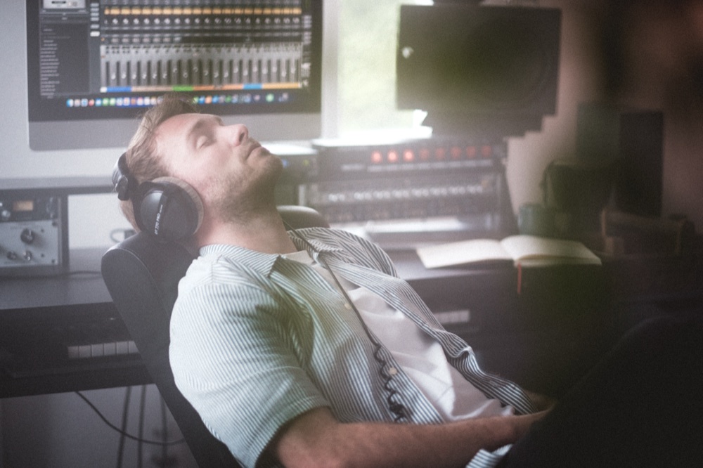 Phil Young hört mit Kopfhörern konzentriert ab, dahinter Bildschirm, Monitor und Outboard-Rack.