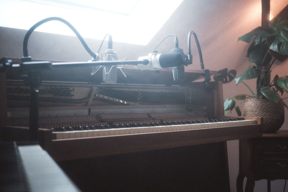 Zwei Mikrofone über dem geöffneten Upright Piano, im Gegenlicht des Dachfensters.